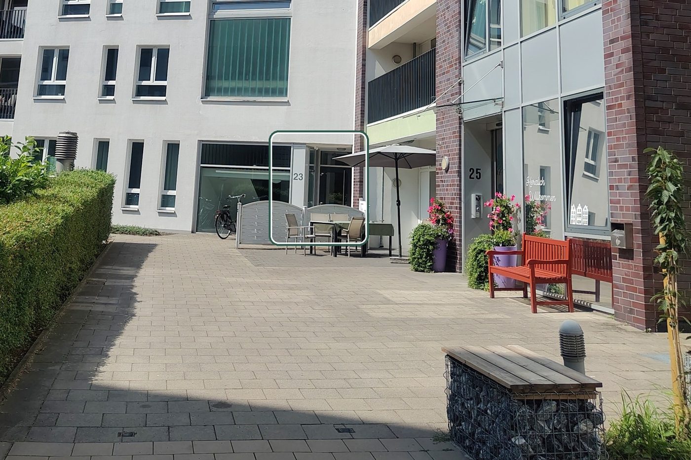View into the courtyard at Pottkamp: on the left the light-coloured building with house number 23, the practice entrance marked in green; on the right the brick building with number 25.